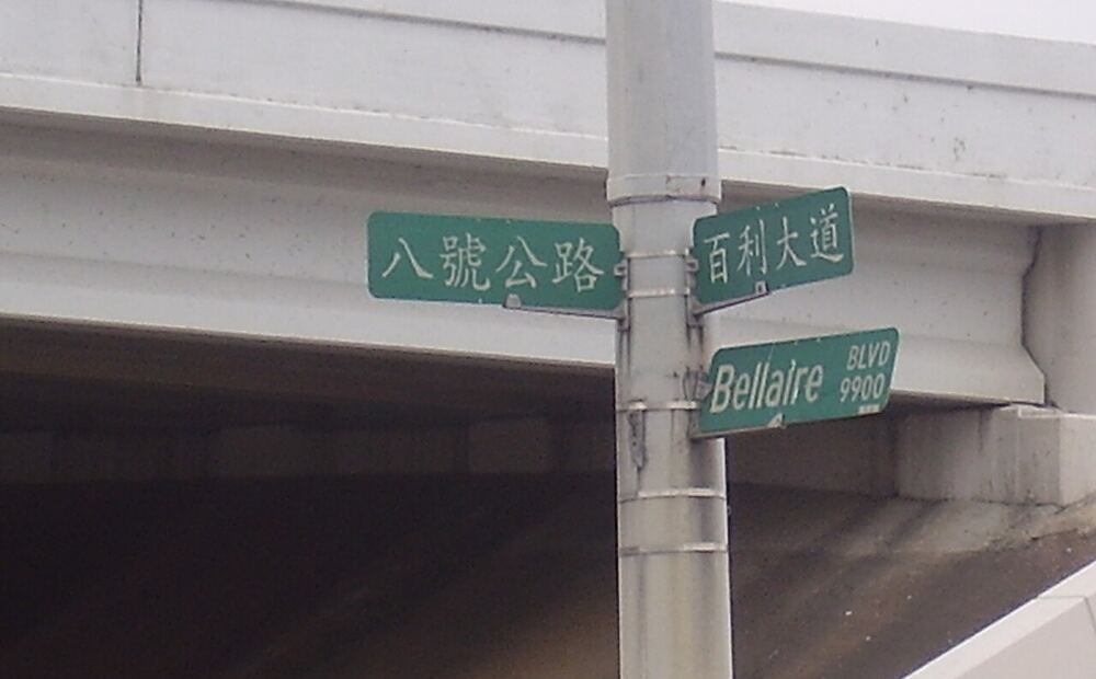休斯顿中国城的中英双语路牌，绿底白字写着「八號公路」「百利大道」与 Bellaire Blvd。